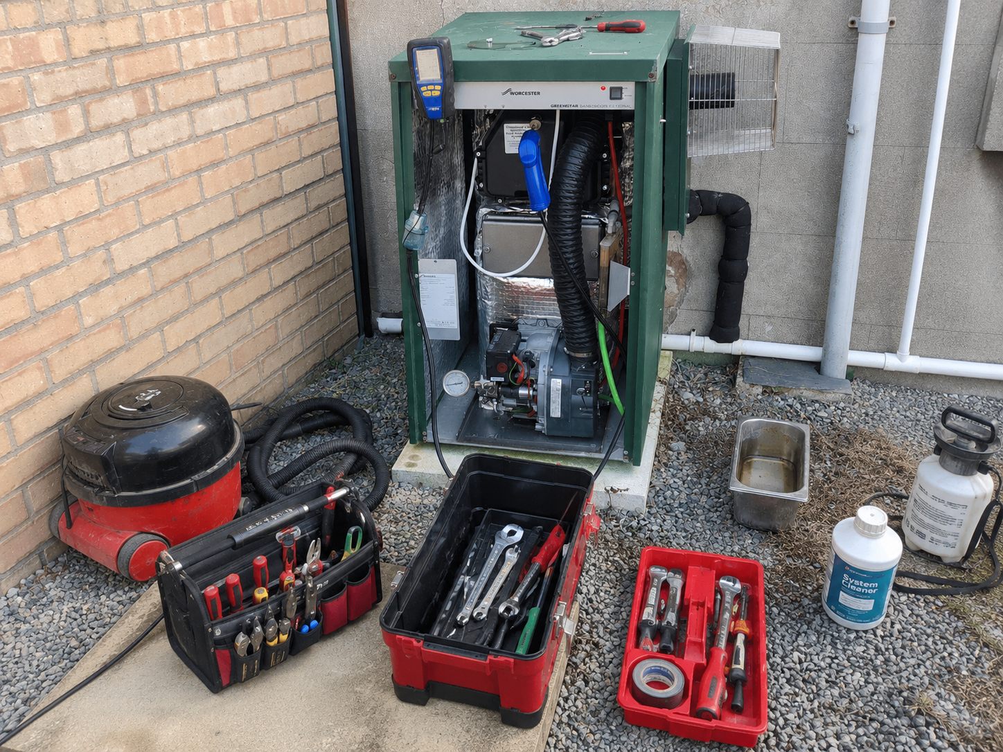 OFTEC engineer servicing an external Worcester oil-fired boiler — burner pulled, flue analyser fitted, tools laid out